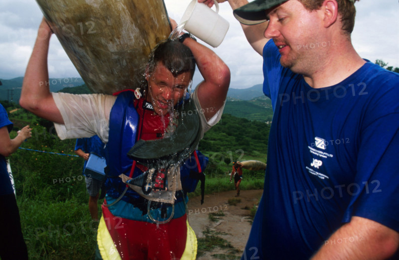 guy pours jug of water over another carrying a canoe