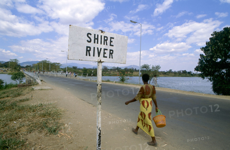 WOMAN WALKING PAST SIGN, SHIRE RIVER, MALAWI