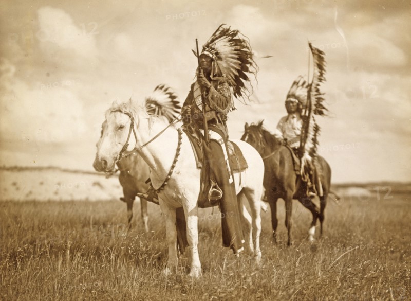 Three Native American chiefs mounted on horses and wearing feather headdresses