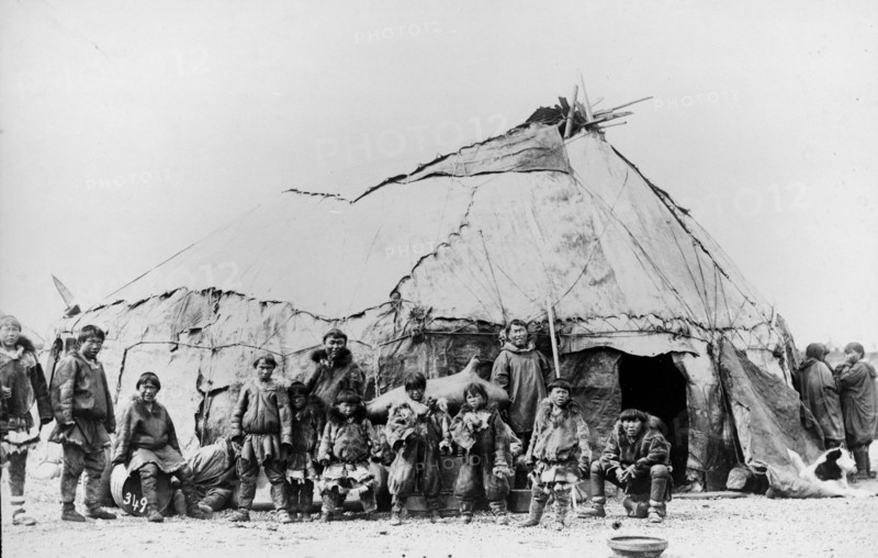 Native American men and children standing in front of a large tent structure