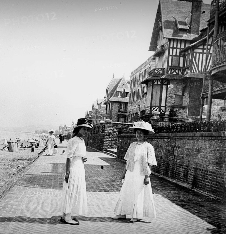 Two young women walk along a promenade by a beach in France, during summer