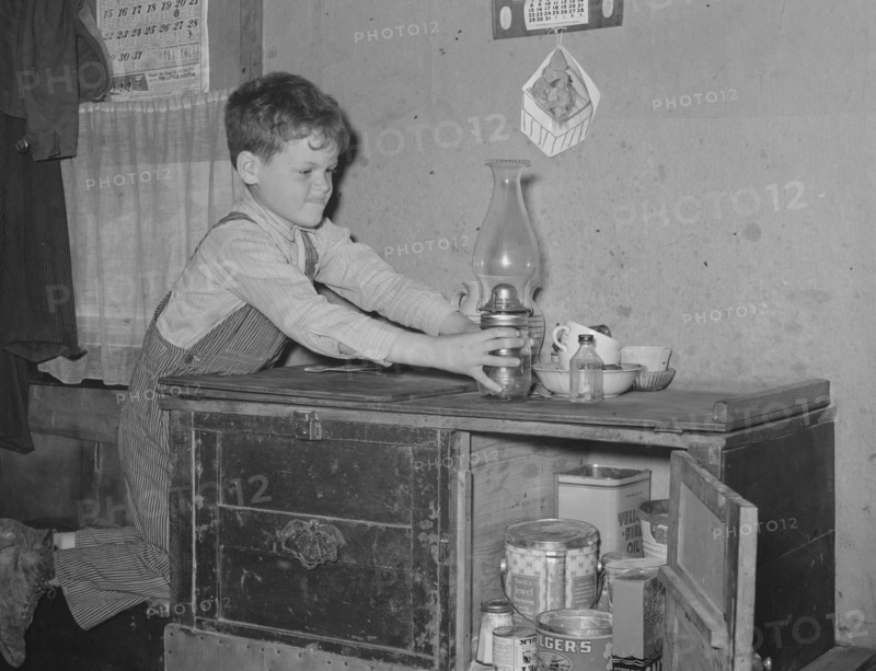 Son of migrant worker reaching for lamp atop cabinet in trailer home. Weslaco, Texas. 19390101