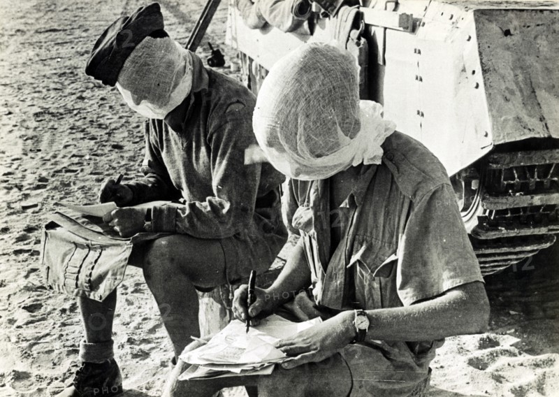 Photographic print of British World War Two soldiers with their heads covered, writing letters beside a tank