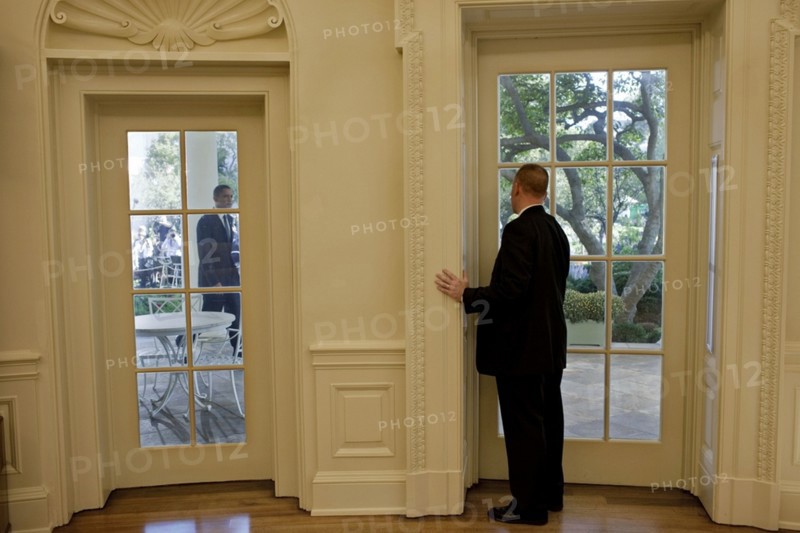 US secret service agent in the oval office, prepares to open a door as President Obama approaches