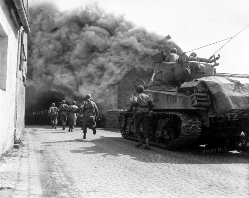Photograph of M4 Sherman tank move through a smoke filled street in Wernberg