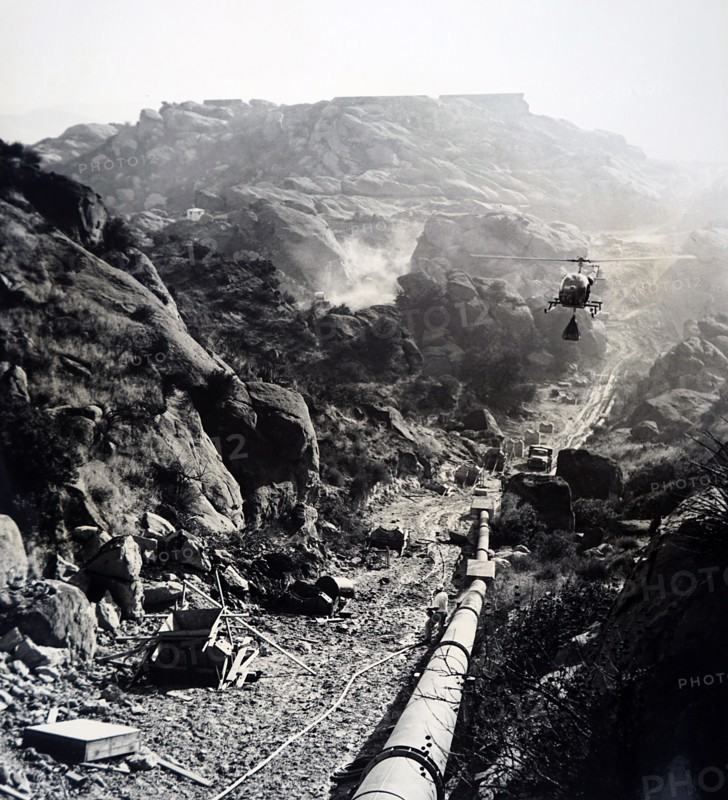 Photograph of helicopter transporting a bag of wet cement to be used in construction in a isolated mountainous area of California