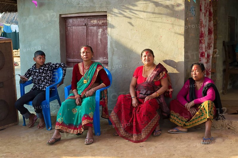 Nepalese women from the Tharu ethnic group sitting in front of a house during a wedding