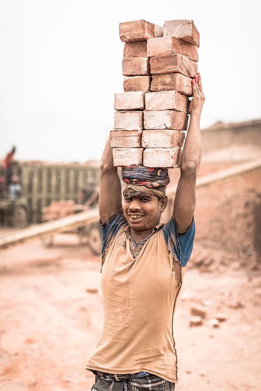 Worker with bricks on his head in the brickyard