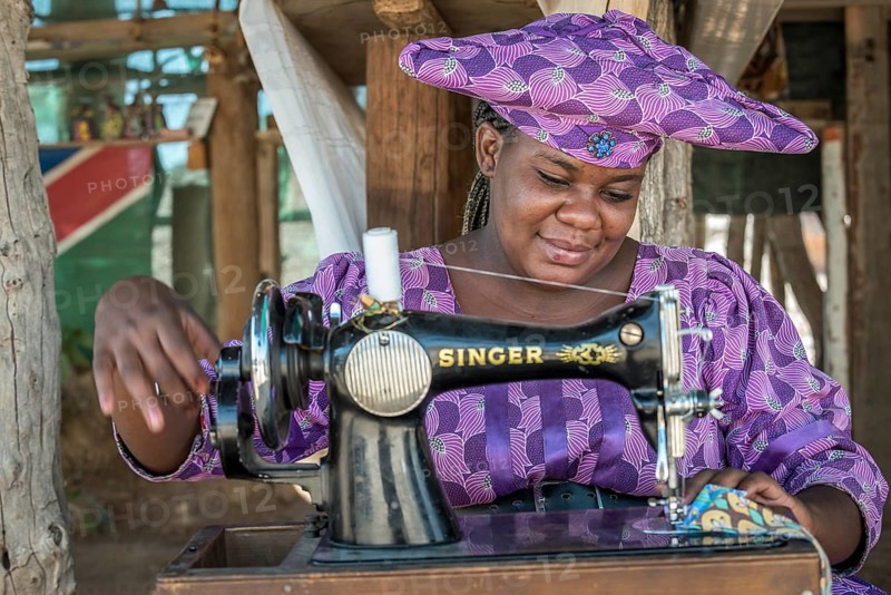 Native Herero woman with typical headgear and clothes is sitting at a sewing machine