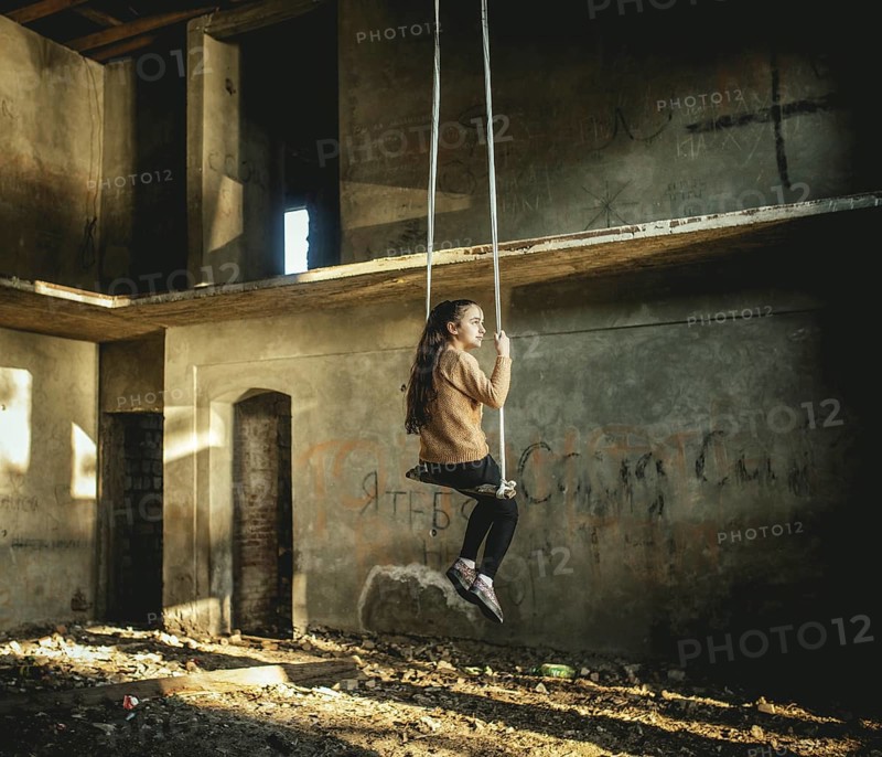 Girl rocking on a swing in a destroyed building on the seafront in Okhamchira