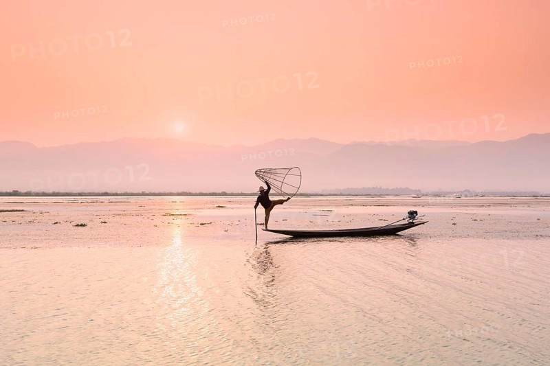 Inle lake fisherman standing on a longtail boat in the distinctive leg rowing stance used by the Intha people