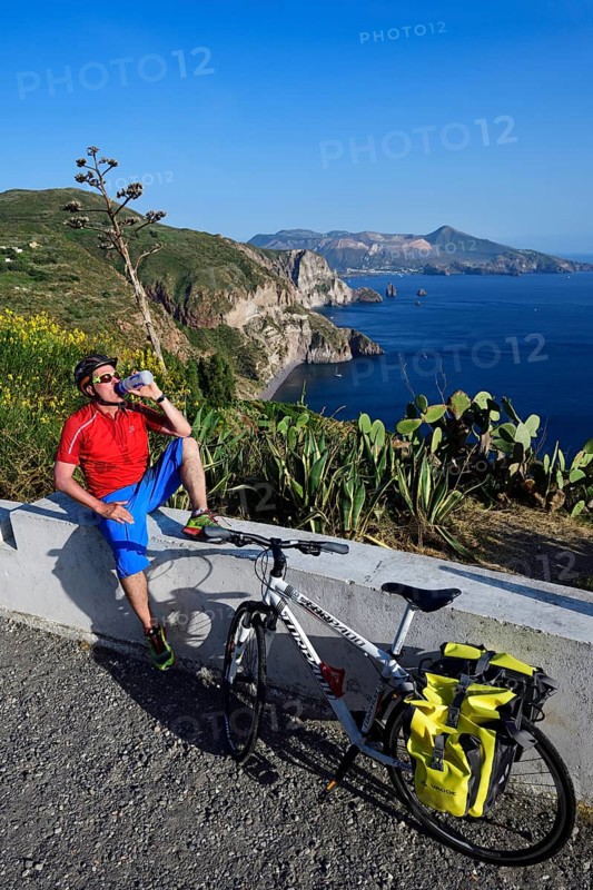 Cyclist pausing on the Belvedere Quattrocchi with a view over the rocks Faraglione on the island Vulcano