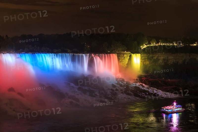 Tourist boat in front of illuminated waterfall