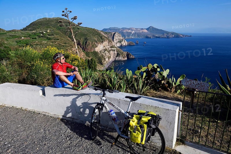 Cyclist pausing on the Belvedere Quattrocchi with a view over the rocks Faraglione on the island Vulcano
