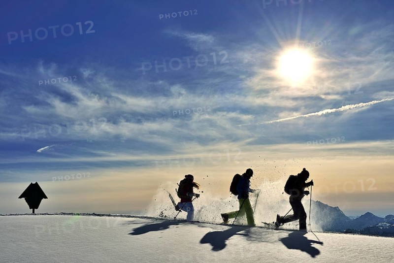 Three snowshoe walkers run in the snow against the light