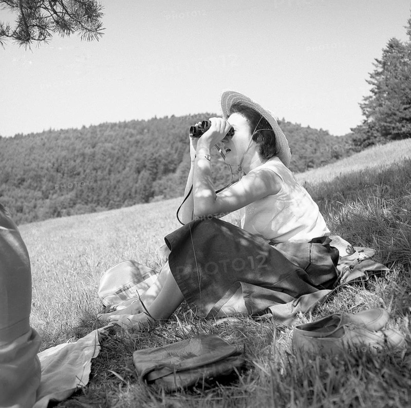 Woman sitting in nature looking through binoculars around 1950