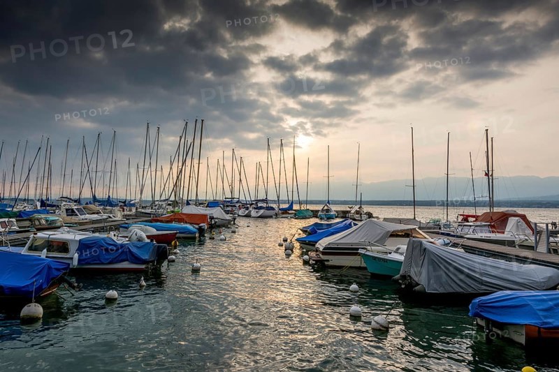 Small boats sheeted and moored along a pontoon on the lake Geneva under a stormy sky