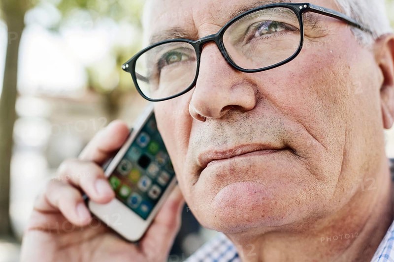 Grey-haired senior with glasses talking on the phone with his smartphone