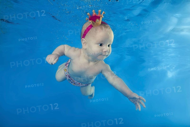 A little girl in a crown swims underwater in the pool