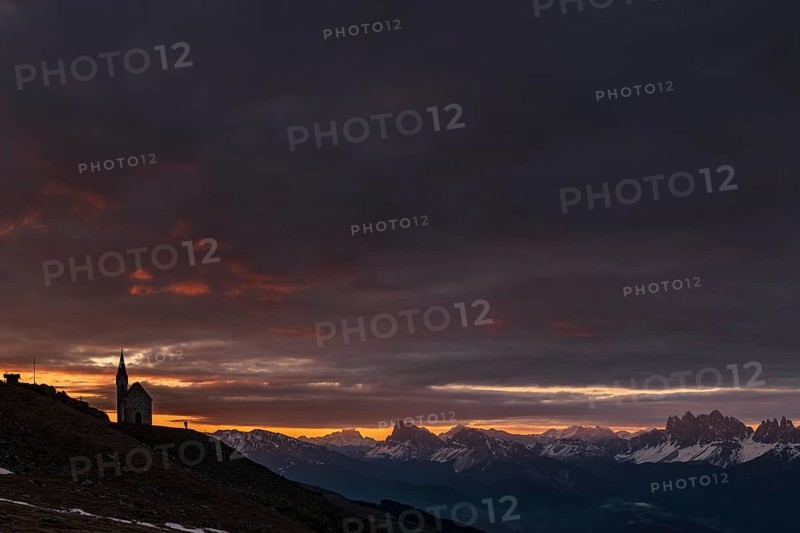 Latzfonser cross chapel at sunrise with dramatic clouds and South Tyrolean mountains