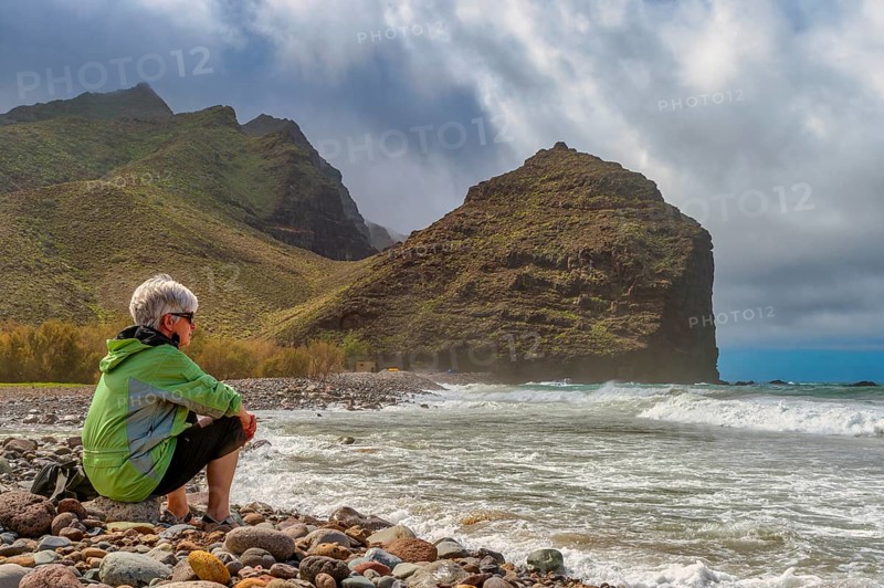 Tourist sits on the beach of Parque Ruben Perez in front of Charco de la Aldea