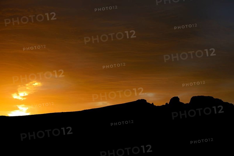Dramatic sunset with rising storm clouds in front of mountain silhouette