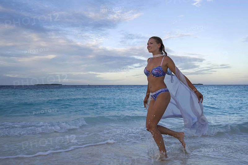 Young woman in bikini running on beach at dusk
