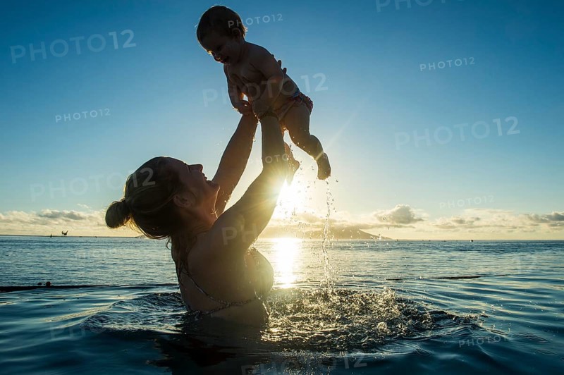 Mother playing with her little baby in the water at sunset