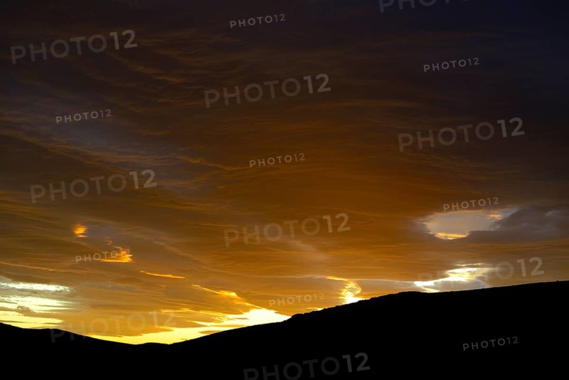 Dramatic sunset with rising storm clouds in front of mountain silhouette