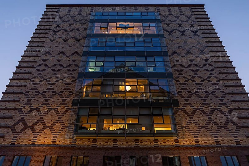 Clinker facade with illuminated rooms from the former egg cold store at dusk