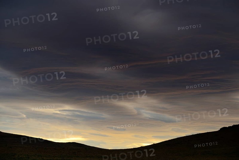 Dramatic sunset with rising storm clouds in front of mountain silhouette