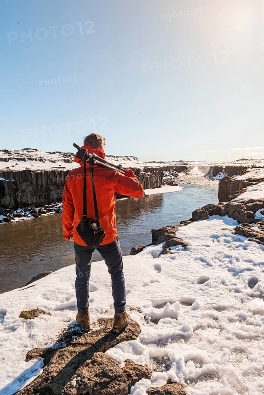 Man with camera equipment looking at Selfoss waterfall in winter