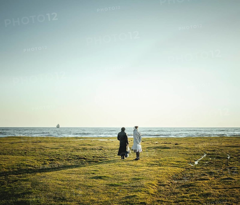 Two women standing at the coast looking at the horizon