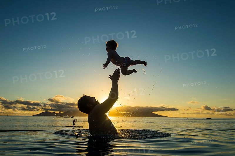 Father playing with his little baby in the water at sunset