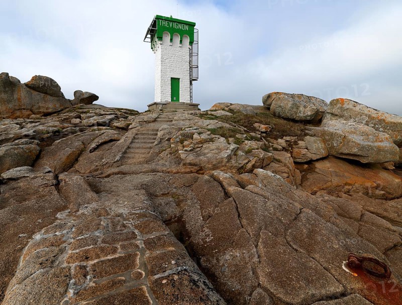 Green and white lighthouse on granite rocks