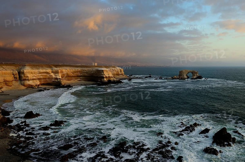 Rocky coast with arch La Portada at sunset with clouds
