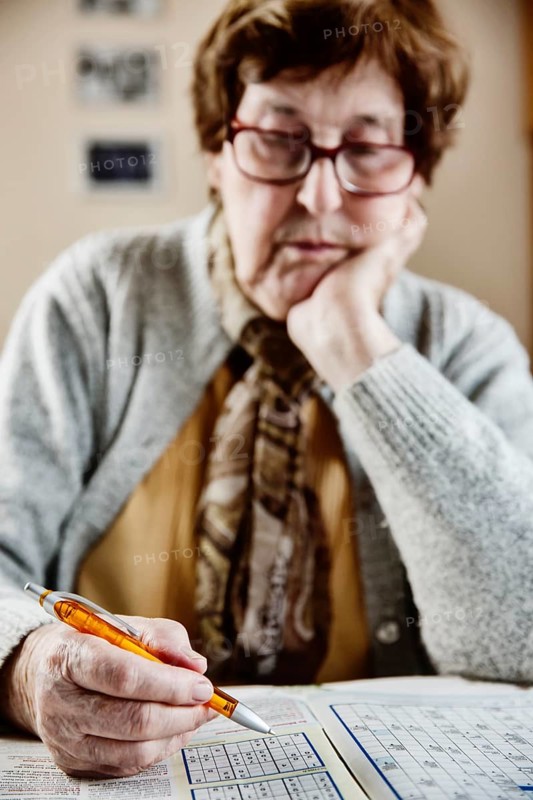 Senior sits at the table at home and solves puzzles