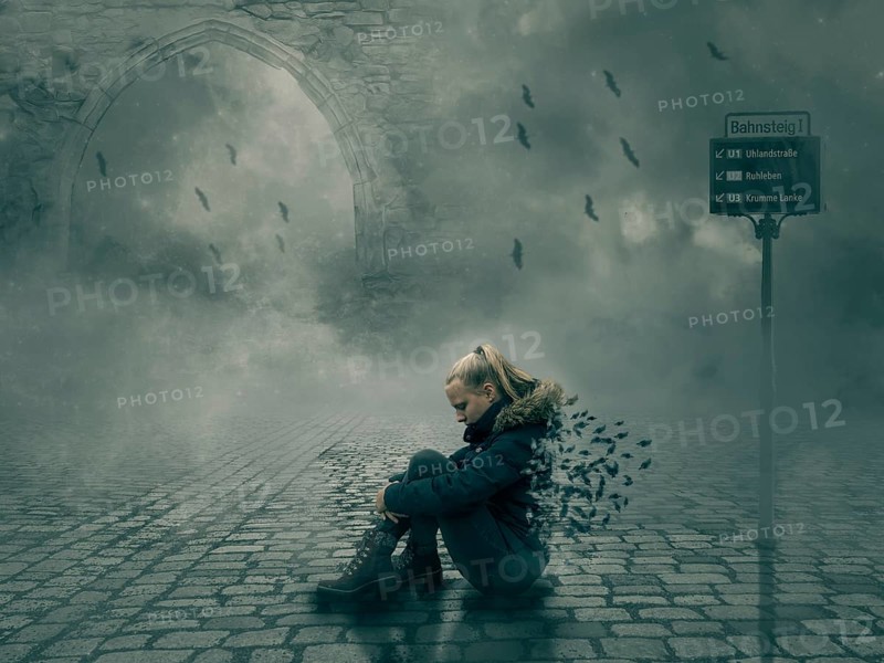 Young woman sitting on cobblestone pavement in surreal and dark fantasy street scene