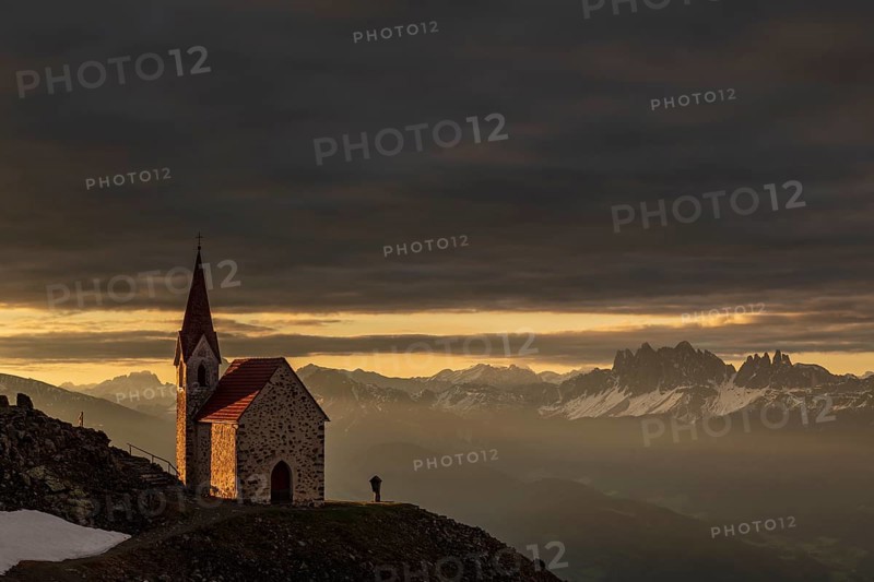 Latzfonser cross chapel at sunrise with dramatic clouds and South Tyrolean mountains