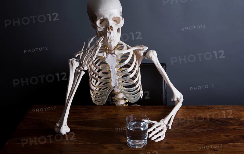Skelett sits at the table with a glass of water in his hand