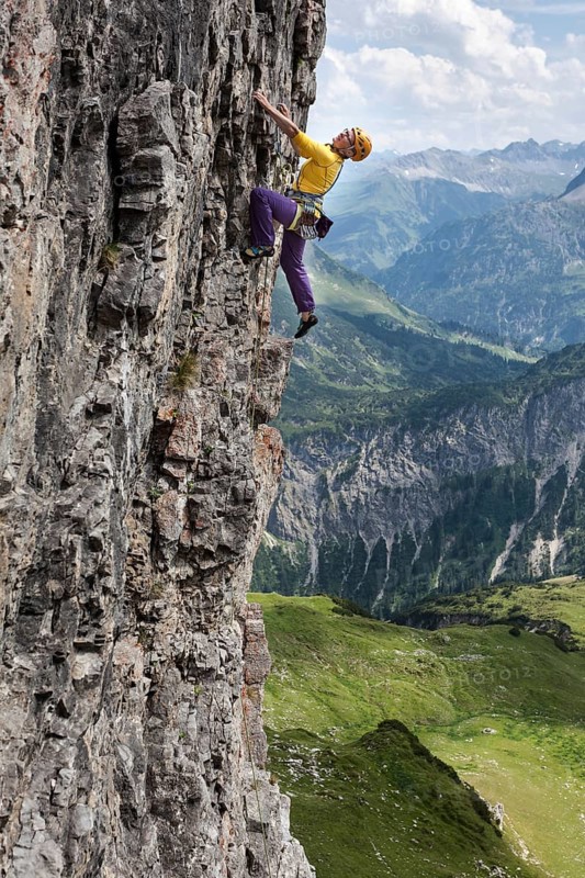 A woman climbs up a vertical rock face