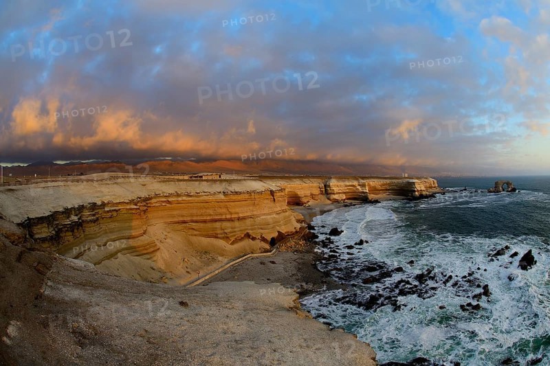 Rocky coast with arch La Portada at sunset with clouds