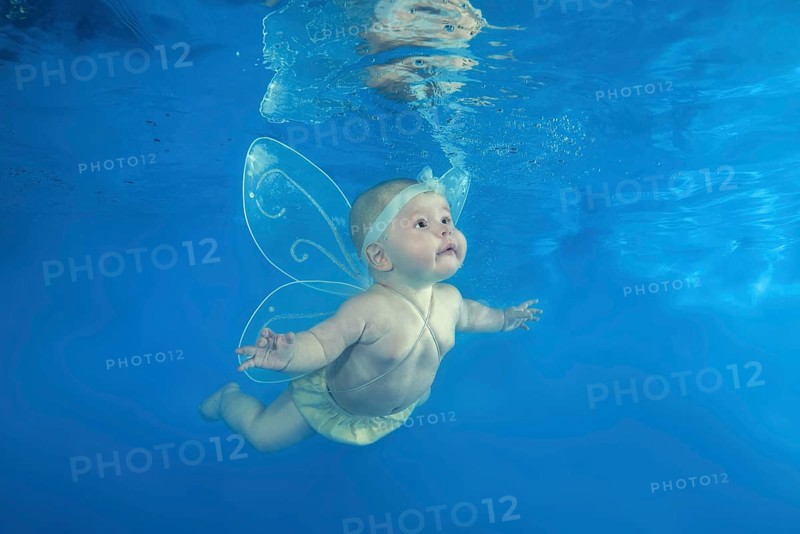 A little girl in a fairy costume swims underwater in the pool