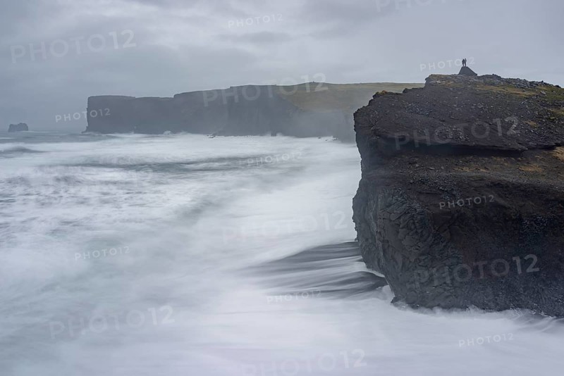Couple stands above the Cliffs of Dyrholey at Storm
