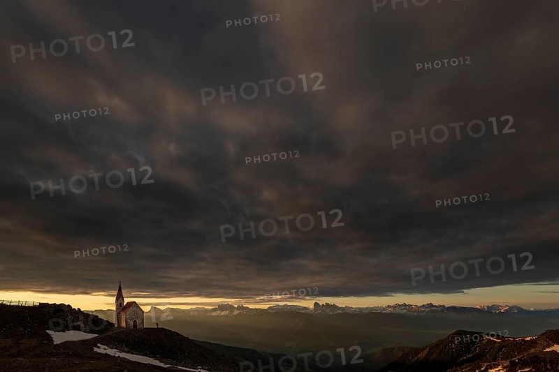 Latzfonser cross chapel at sunrise with dramatic clouds and South Tyrolean mountains