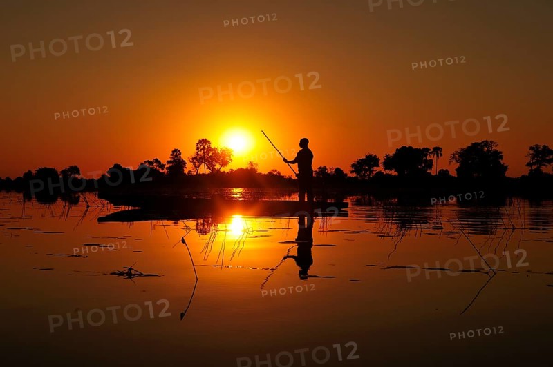 Local bargeman sails in traditional Mokoro dugout boat at sunset