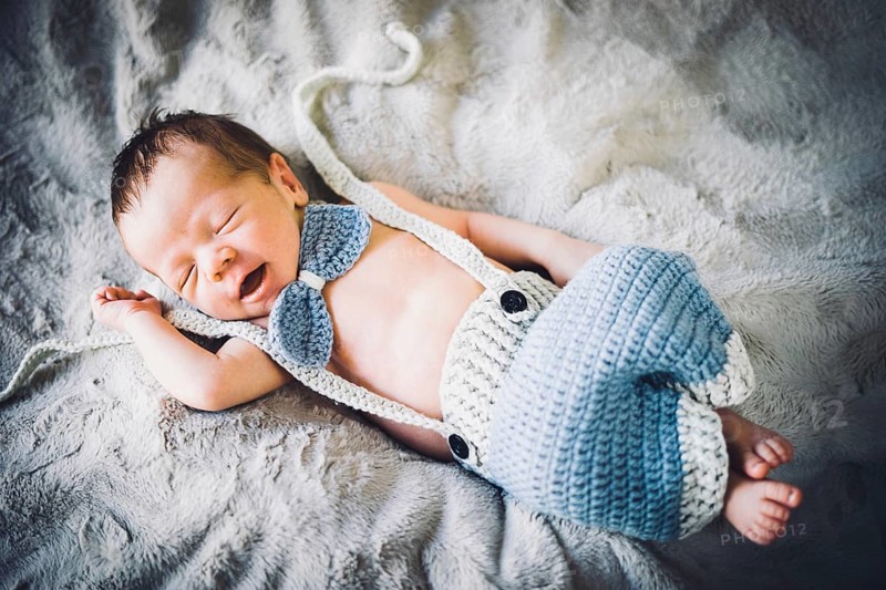 A newborn baby boy sleeping in blue and grey knitted bow tie and trousers