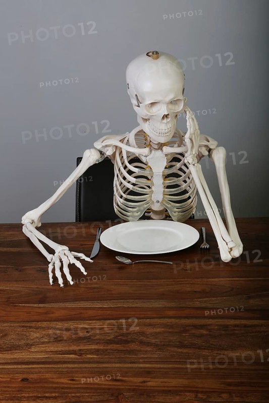 Skeleton with supported head sitting at table