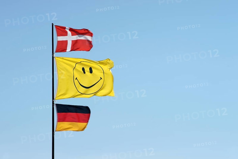 German and Danish flags waving together with a smiley flag on a flagpole