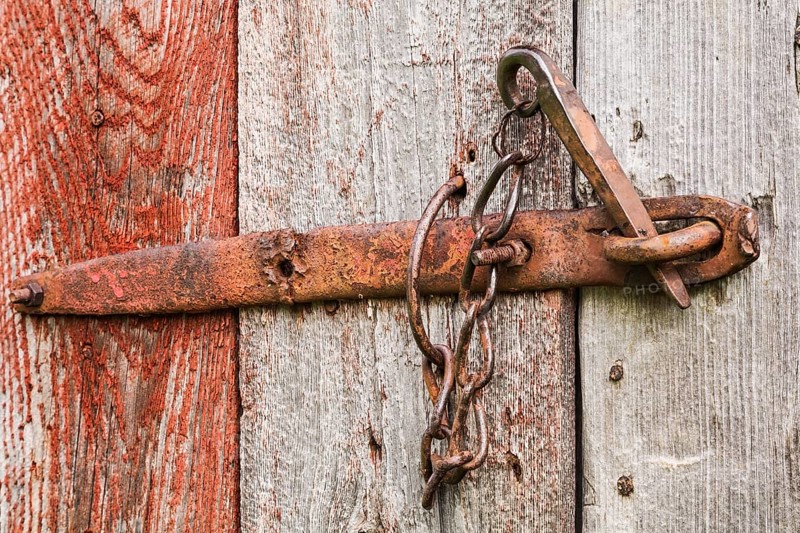 Close-up of rusted steel latch on old wooden grey and red painted barn door